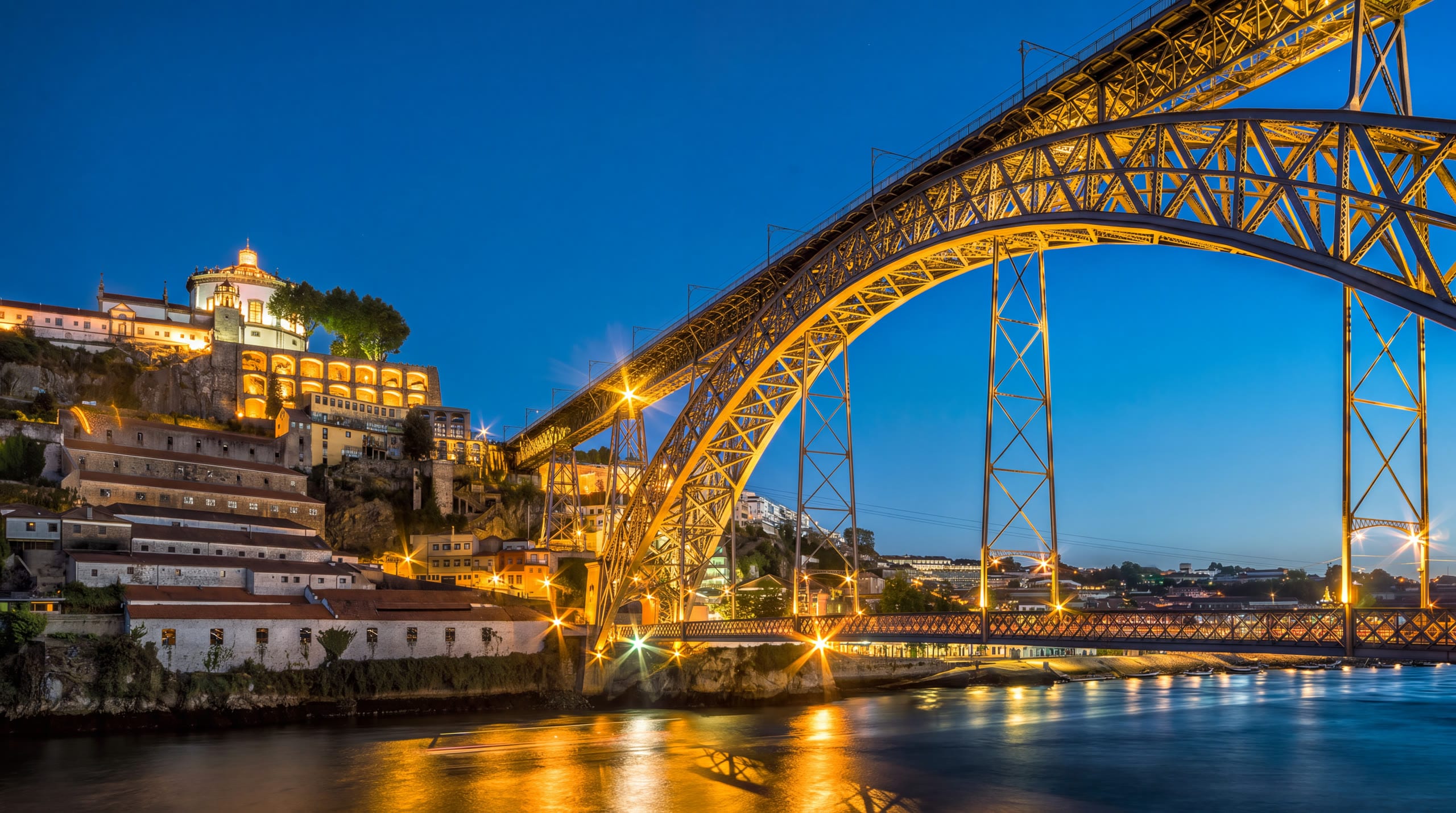 Ponte Dom Luís I iluminada sobre o rio Douro à hora azul, com o Porto ao fundo