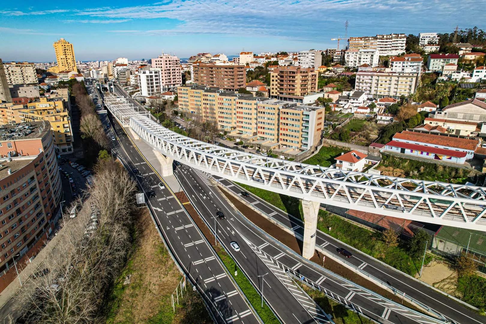Vista aérea do viaduto da Linha Amarela do Metro do Porto sobre a avenida, entre prédios de habitação