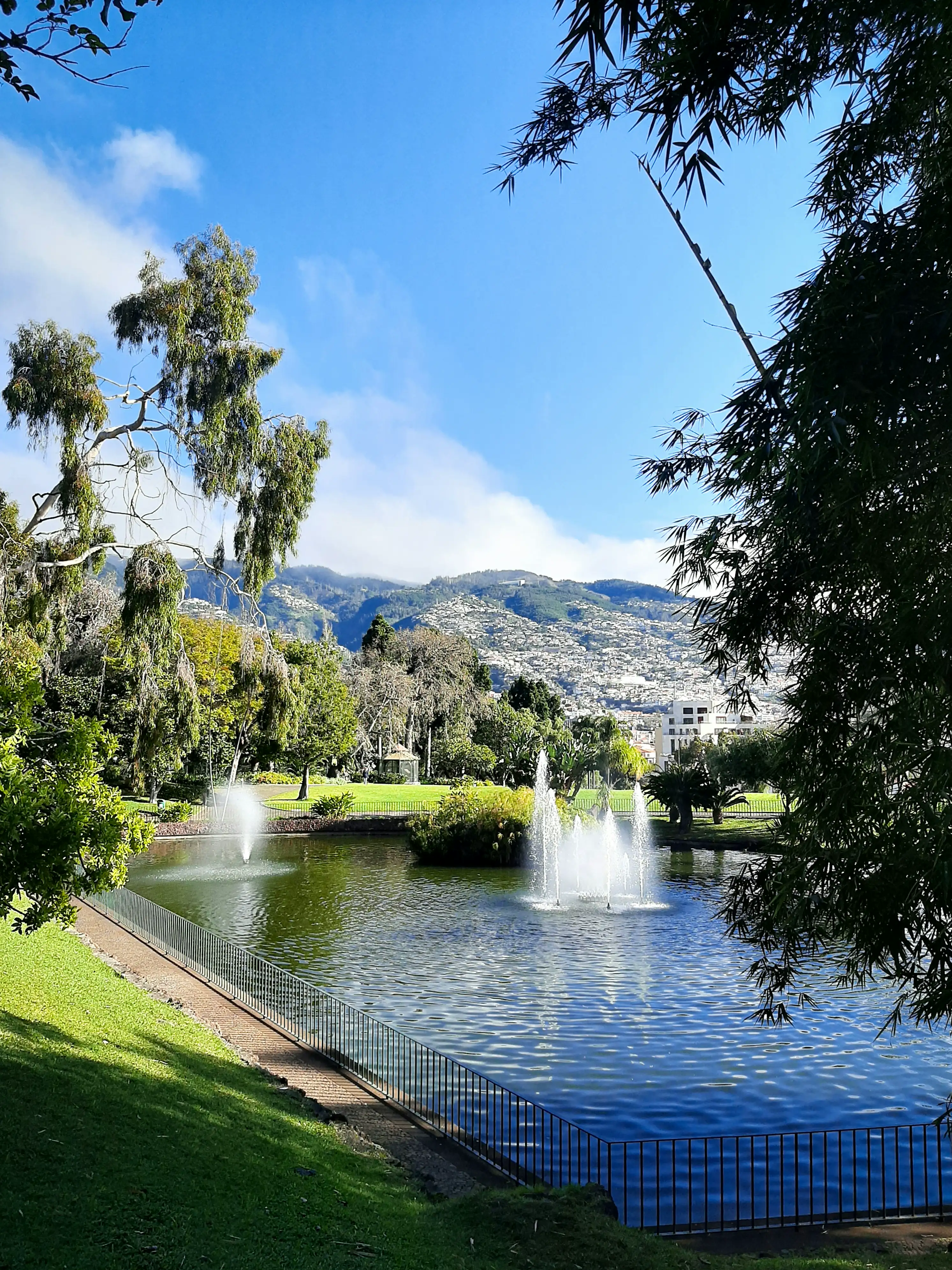 Parque da cidade com lago e repuxos, montanhas ao fundo